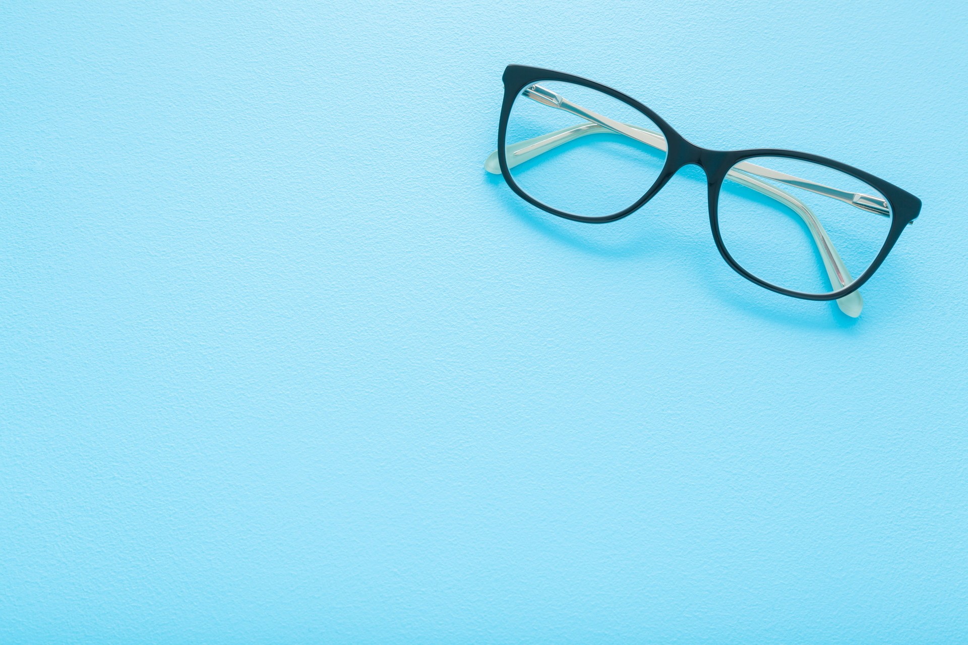 Eyeglasses with dark black plastic frame on light blue table background. Pastel color. Closeup. Empty place for text. Top down view.